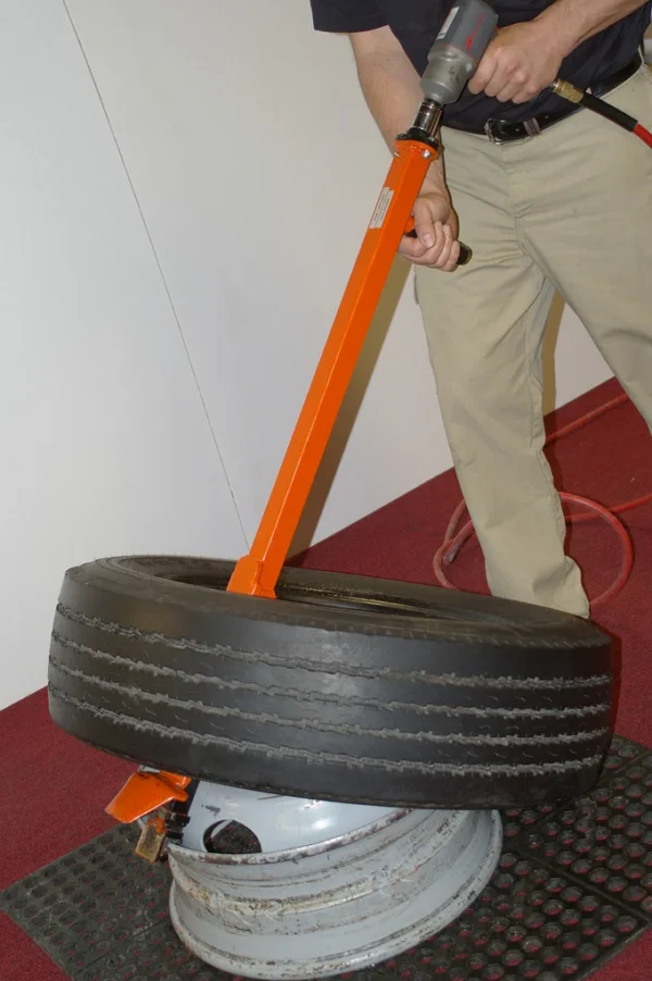 Technician using the Pneu-Tek Impact Demounter to remove a standard vehicle tire with air-powered assistance